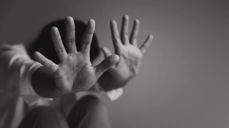 Manos de un niño en blanco y negro, con las manos de un adulto detrás, en un gesto que simboliza la vulnerabilidad y la necesidad de protección.